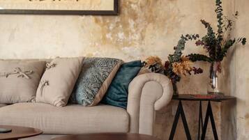 A living room with a sofa, a coffee table, a side table with a vase of flowers, and a wall with a framed piece of calligraphy.