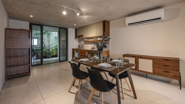 Área de refeições moderna com mesa posta para quatro, cozinha ao fundo e porta de vidro deslizante para um jardim.