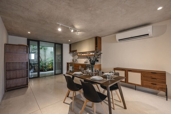 Un'area pranzo moderna con tavolo apparecchiato per quattro, una cucina sullo sfondo e una porta vetrata scorrevole che dà su un giardino.