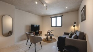 Uma sala de estar moderna com televisão de tela plana, sofá, poltrona, mesinha com um vaso e luminária de chão.