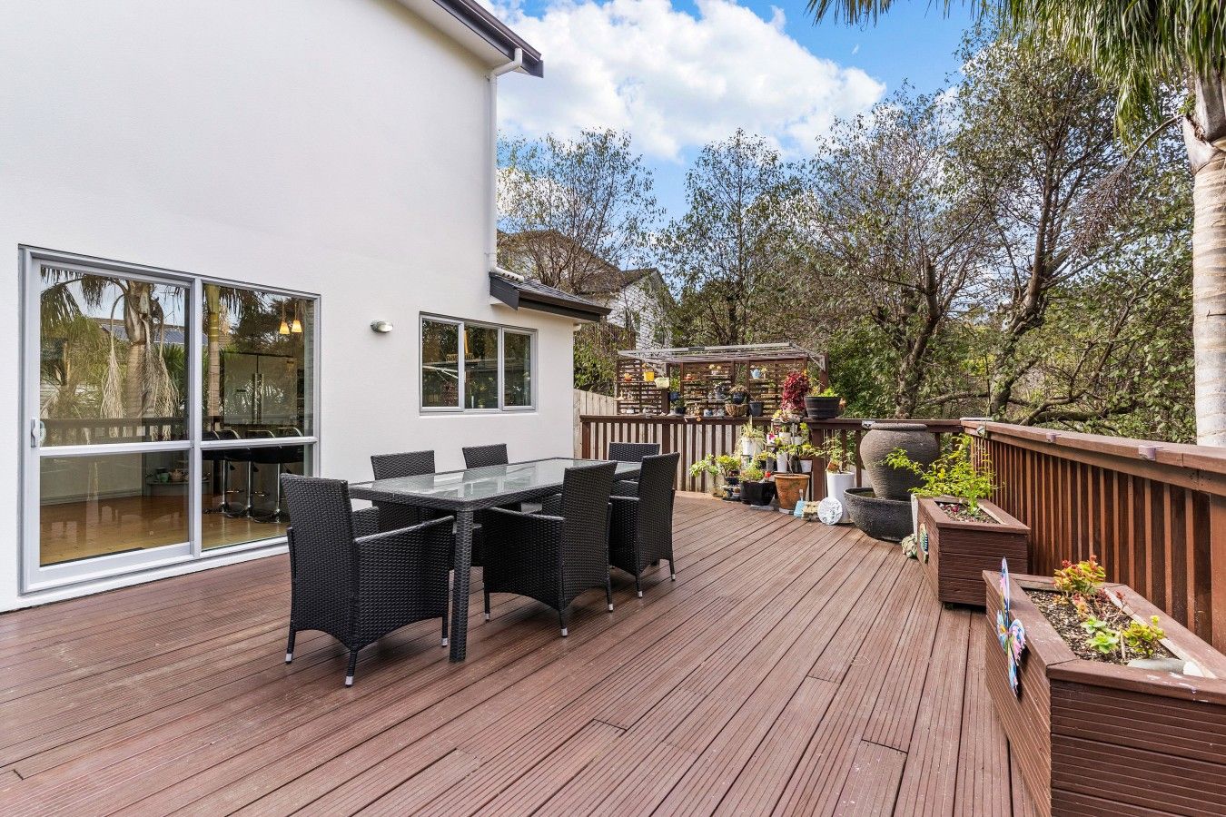 Une terrasse dotée d’une table et de chaises, entourée de plantes en pot et d’une clôture en bois.