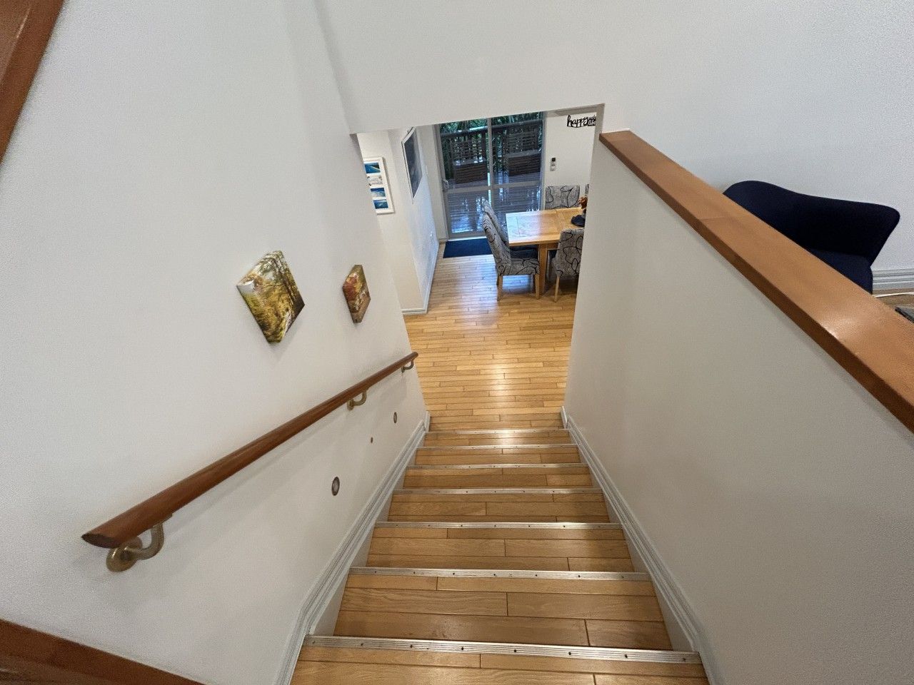 Een houten trap met een leuning, die leidt naar een eetgedeelte met een tafel en stoelen.