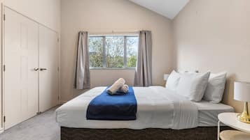 Een hotelkamer met een bed, een raam met gordijnen, een nachtkastje met een lamp en een deur.