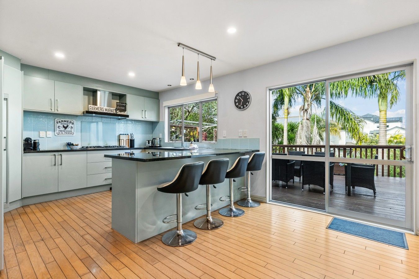 A modern kitchen with a central island, bar stools, and a view of a deck with outdoor furniture.
