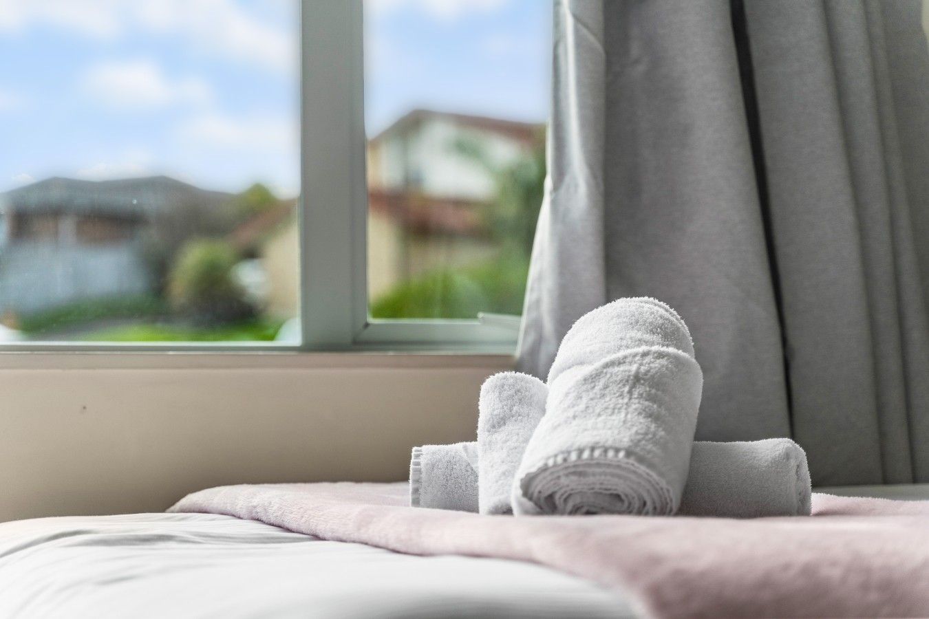 A bed with a white blanket and two rolled towels placed on it.