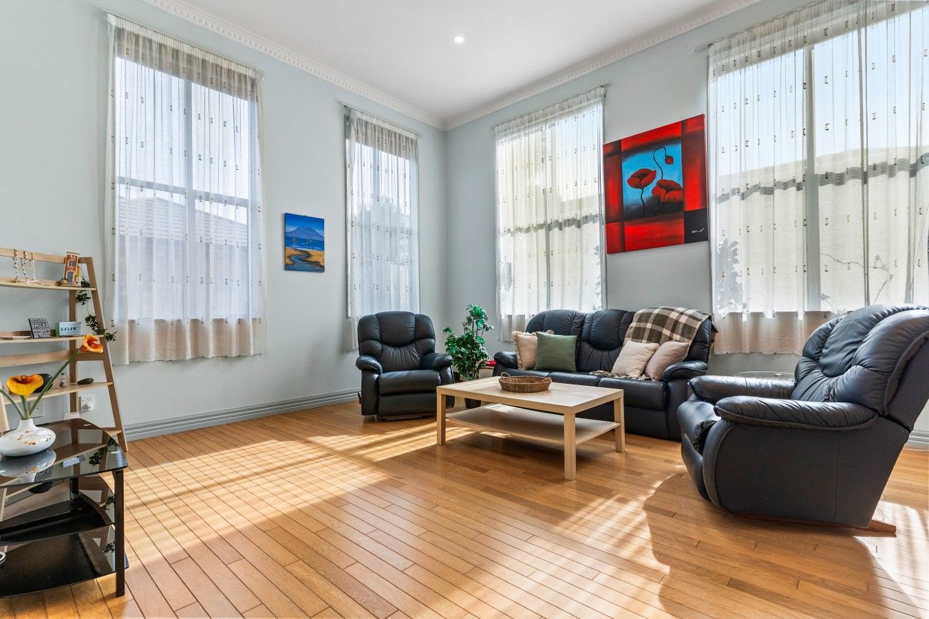 A spacious living room with a wooden floor, a black leather sofa, a black leather armchair, and a wooden coffee table.