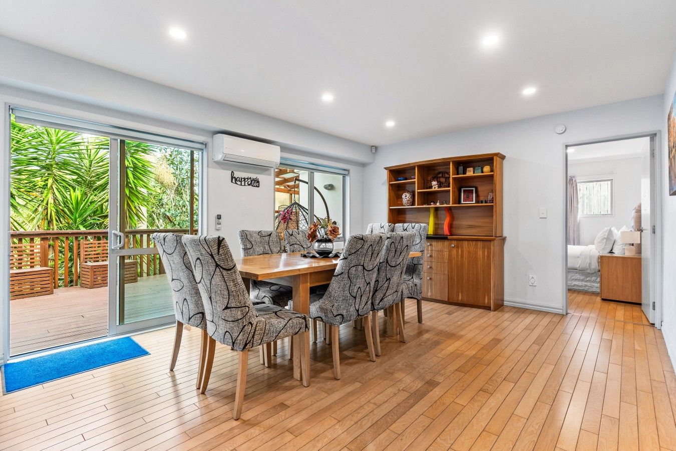 Un comedor moderno con mesa de madera y sillas estampadas, unidad de aire acondicionado empotrada y un mueble de madera con estantes.
