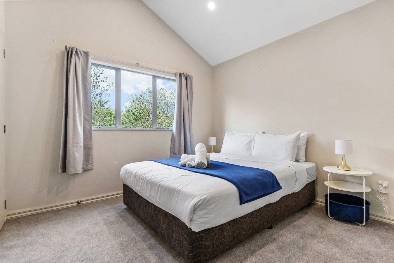 A bedroom with a large bed, a bedside table with a lamp, and a window with curtains.