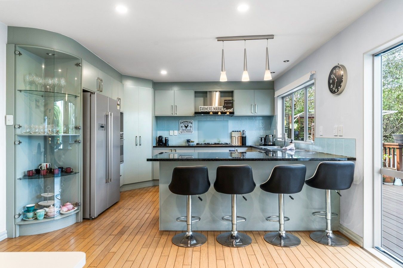 Een moderne keuken met een centraal eiland, barstoelen en een glazen vitrinekast.