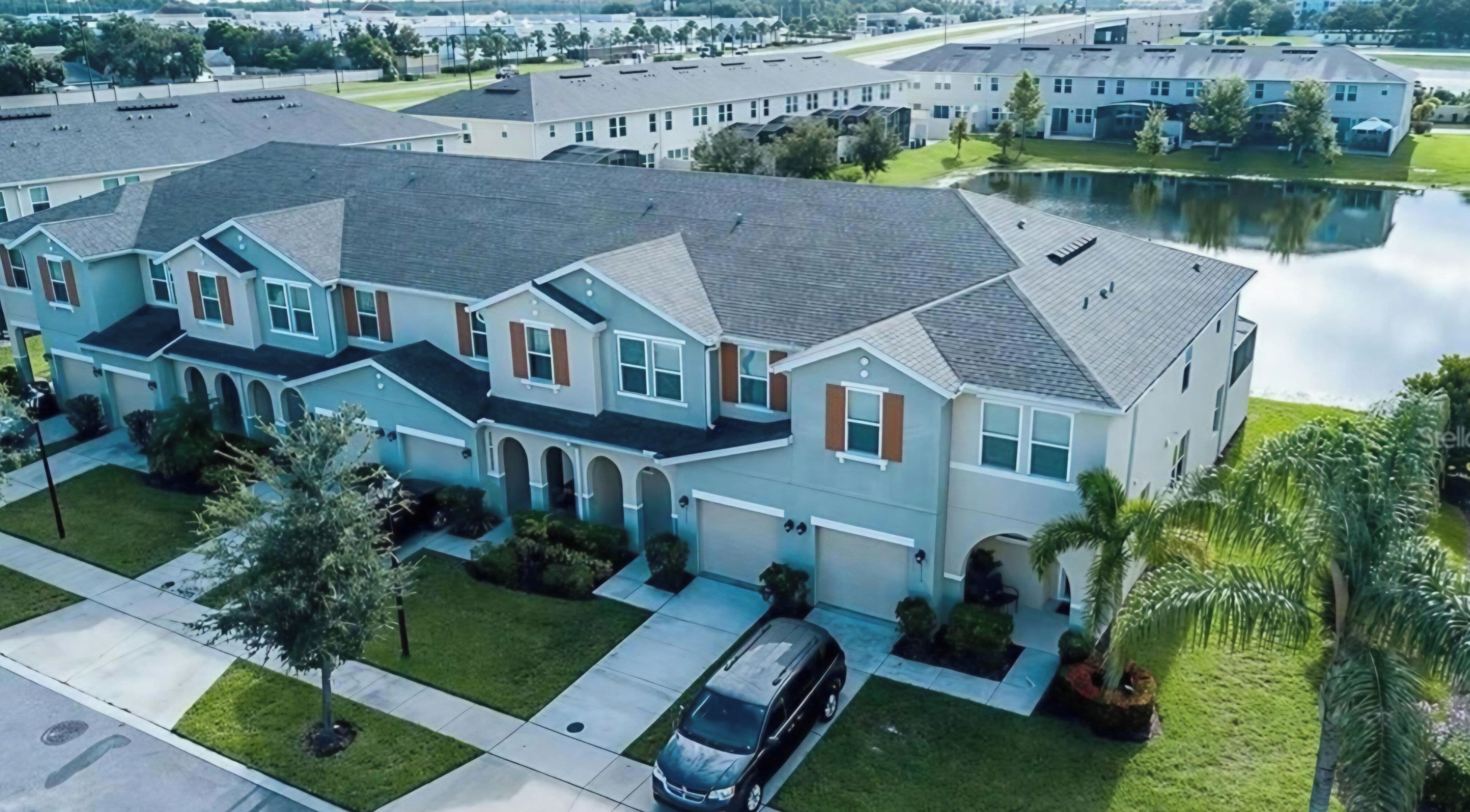 A multi-story residential building with a driveway, a car parked in the driveway, and a body of water in the background.