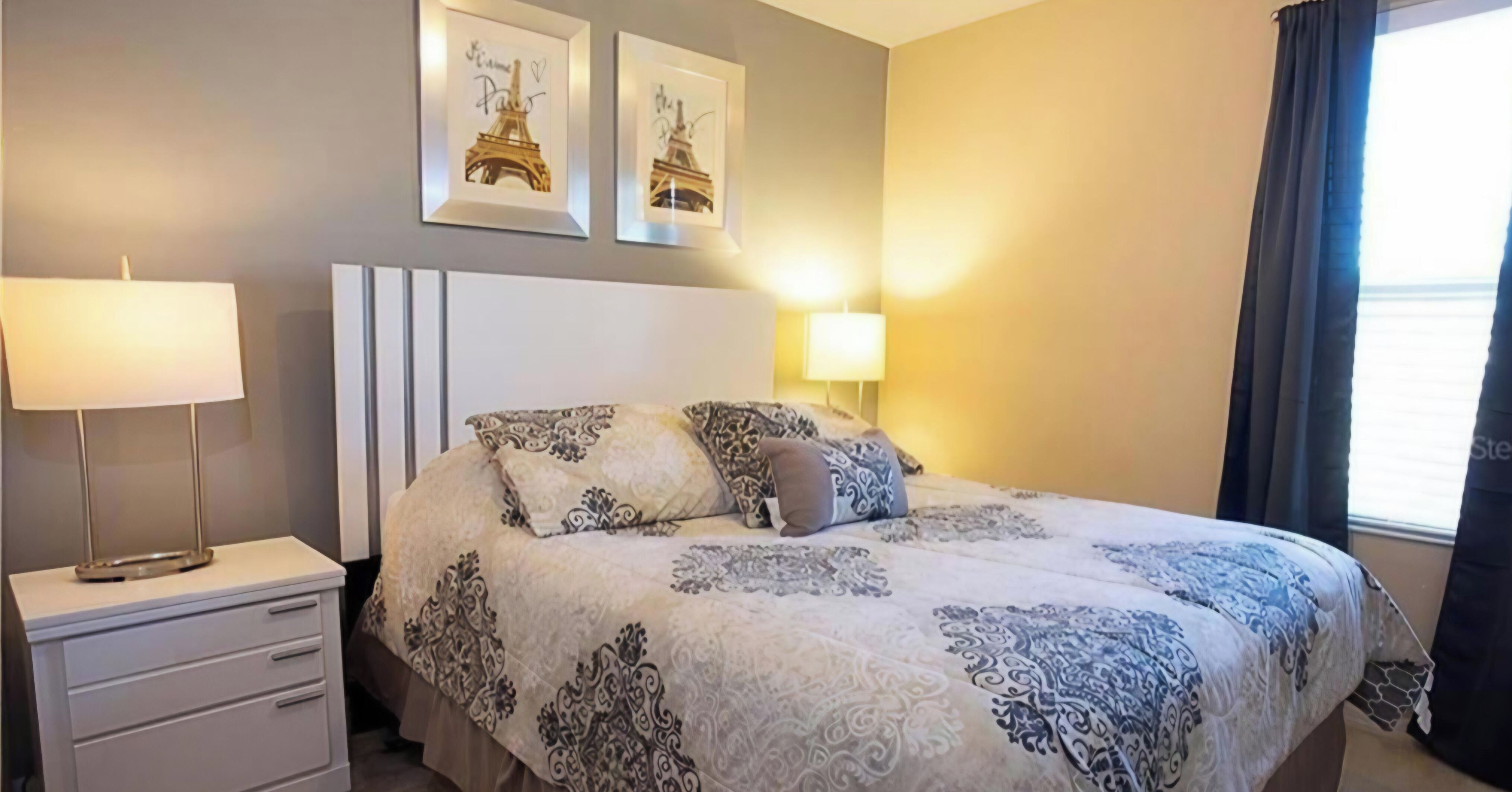 A hotel room with a bed, bedside tables, a lamp, and two framed pictures of the Eiffel Tower.