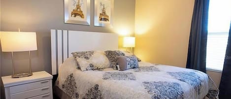 Habitación de hotel con cama, mesitas de noche, lámpara y dos cuadros con imágenes de la Torre Eiffel.