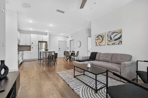 A modern living room with a grey sofa, a coffee table, and a dining area with chairs and a table. - Cozy 2 BR Apt |King Bed |Pool |Gym| Close to Mayo. (Jacksonville)