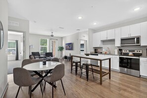 A modern kitchen with white cabinets, a central island, and a dining area with chairs. - Cozy 2 BR Apt |King Bed |Pool |Gym| Close to Mayo. (Jacksonville)
