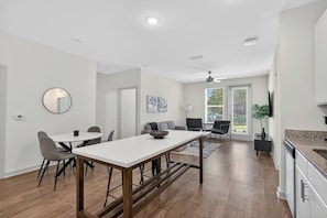 Eine moderne Küche mit einer Granit Arbeitsplatte, ein Essbereich mit einem weißen Tisch und Stühlen sowie ein Wohnbereich mit einer Couch und einem Couchtisch.