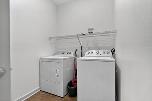 Ein Waschraum mit einer Waschmaschine und einem Trockner, einem Wäscheständer und einem roten Eimer.