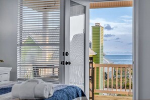 A bedroom with a view of the ocean, a balcony with a railing, and a door with a window. - Bikini Bottom · New Listing! Steps to Beach, Gulf-View Porches & Pool (Gulf Shores)