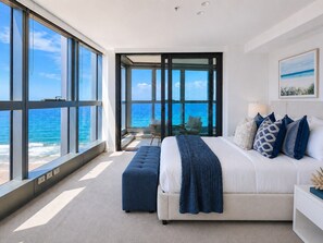 Quarto com uma grande janela com vista para o oceano, cama com manta azul e vista do mar.