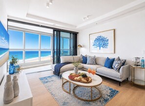 A modern living room with a large window, a sofa, a coffee table with a fruit platter, and a painting on the wall. - Harmony Oceanview 2BR Suite | Jewel + Parking (Surfers Paradise)