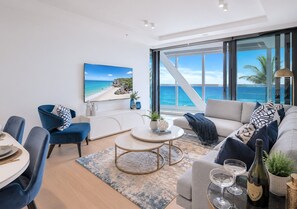 Un salon moderne doté d’une grande fenêtre, d’un coin repas avec des chaises bleues et d’un canapé agrémenté de coussins décoratifs.