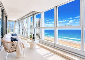 A balcony with a view of the beach, a wicker chair, a small table with a bottle and glasses, and a cityscape in the background. - Harmony Oceanview 2BR Suite | Jewel + Parking (Surfers Paradise)