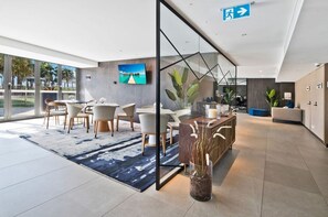 Um saguão moderno de hotel com balcão de recepção, área de estar e uma grande janela com vista para o exterior.