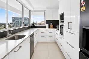 A modern kitchen with a large window, white cabinetry, and a view of a cityscape. - Beachfront Surfers Paradise Apartment - Stunning Ocean Views (Surfers Paradise)