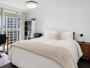 A bedroom with a bed, a desk, a chair, a bookshelf, and a window with a view of buildings. - Beachfront Surfers Paradise Apartment - Stunning Ocean Views (Surfers Paradise)