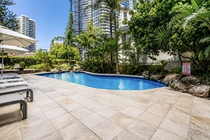 A swimming pool with lounge chairs, surrounded by greenery and tall buildings. - Beachfront Surfers Paradise Apartment - Stunning Ocean Views (Surfers Paradise)