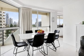 A modern dining area with a white table, black chairs, and a fruit bowl. - Beachfront Surfers Paradise Apartment - Stunning Ocean Views (Surfers Paradise)