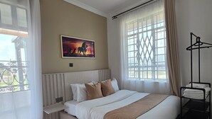 Une chambre à coucher avec un grand lit, une table de chevet, un radiateur, une fenêtre avec des rideaux et un tableau accroché au mur.