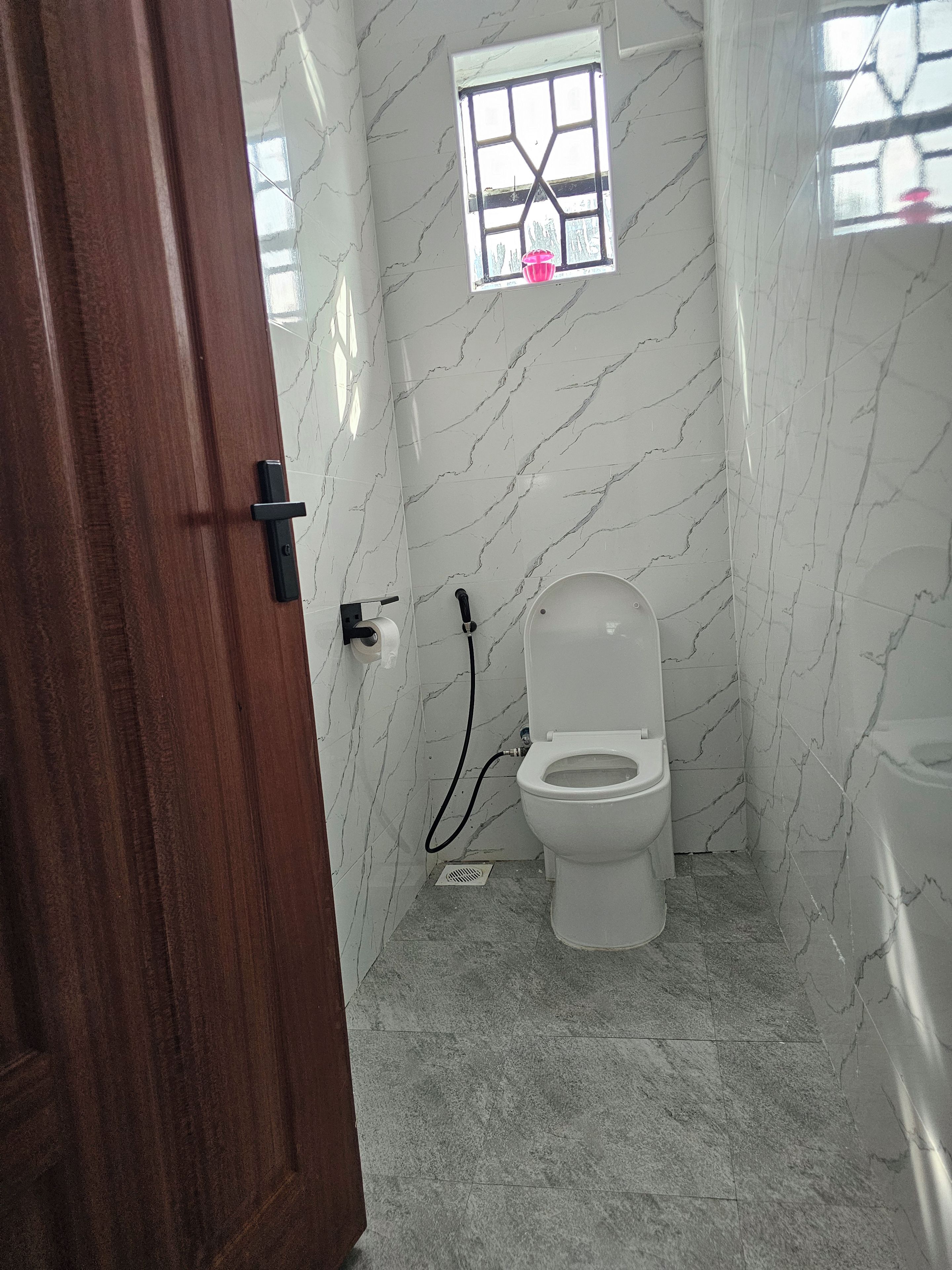 A bathroom with a toilet, a small window, and a shower area.