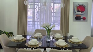Une salle à manger avec une table mise pour six personnes, entourée de chaises, et un vase de fleurs placé au centre.