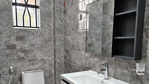 Une salle de bain moderne avec un mur en marbre, des toilettes blanches, un grand lavabo avec un miroir et un meuble à pharmacie noir.