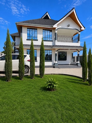 A two-story house with a balcony, a driveway, and a lawn with trees.