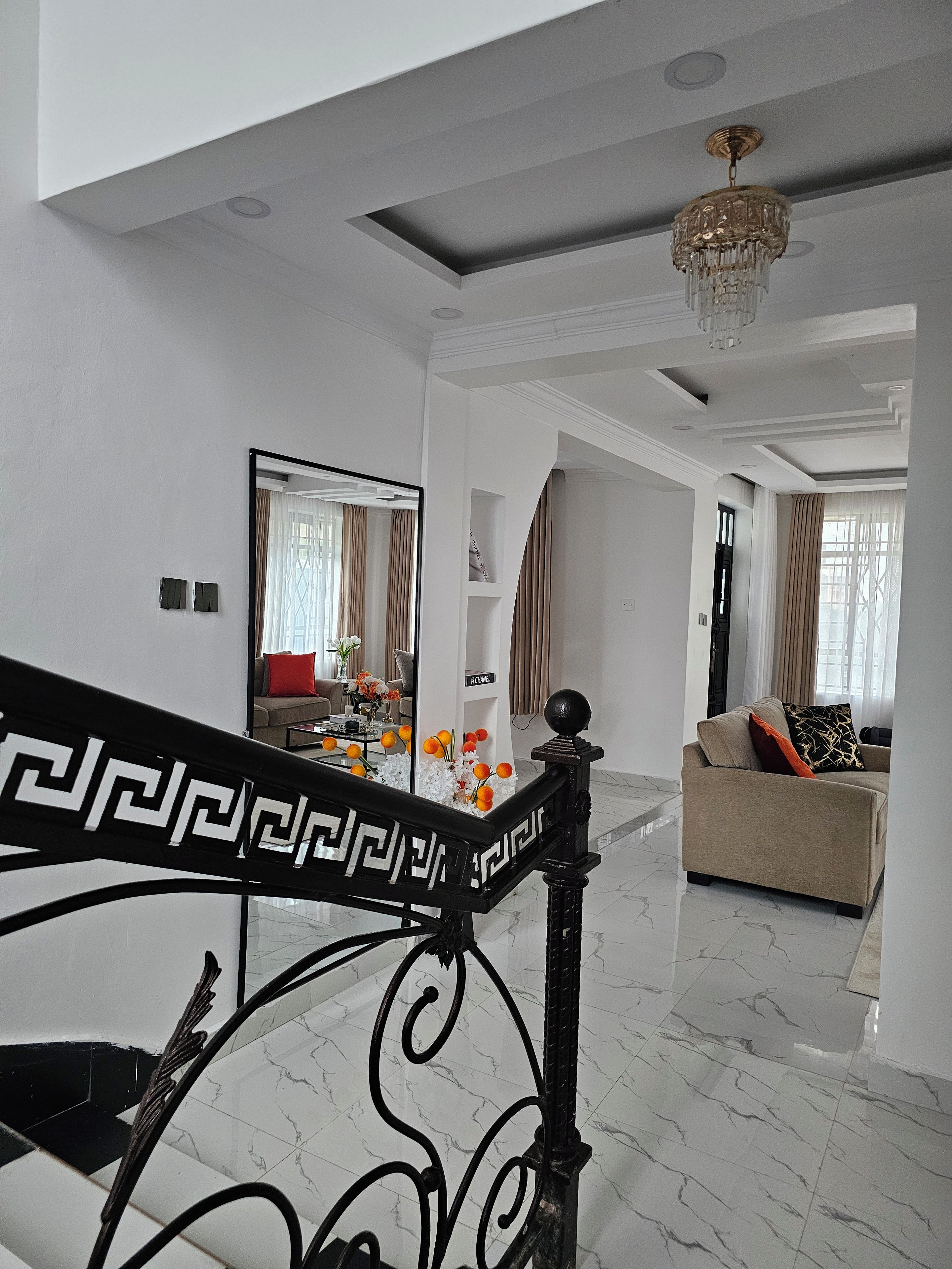 A modern living room with a marble floor, a sofa with cushions, a coffee table with flowers, and a staircase with a decorative railing.