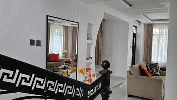 A modern living room with a marble floor, a sofa with cushions, a coffee table with flowers, and a staircase with a decorative railing.