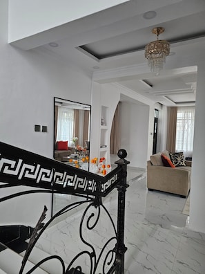 A modern living room with a marble floor, a sofa with cushions, a coffee table with flowers, and a staircase with a decorative railing.