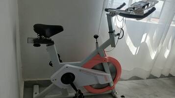 A stationary exercise bike with a digital display, positioned in a room with a tiled floor and a window with sheer curtains.