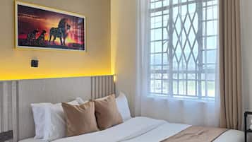 A hotel room with a large bed, a headboard, a window with curtains, and a wall-mounted painting.