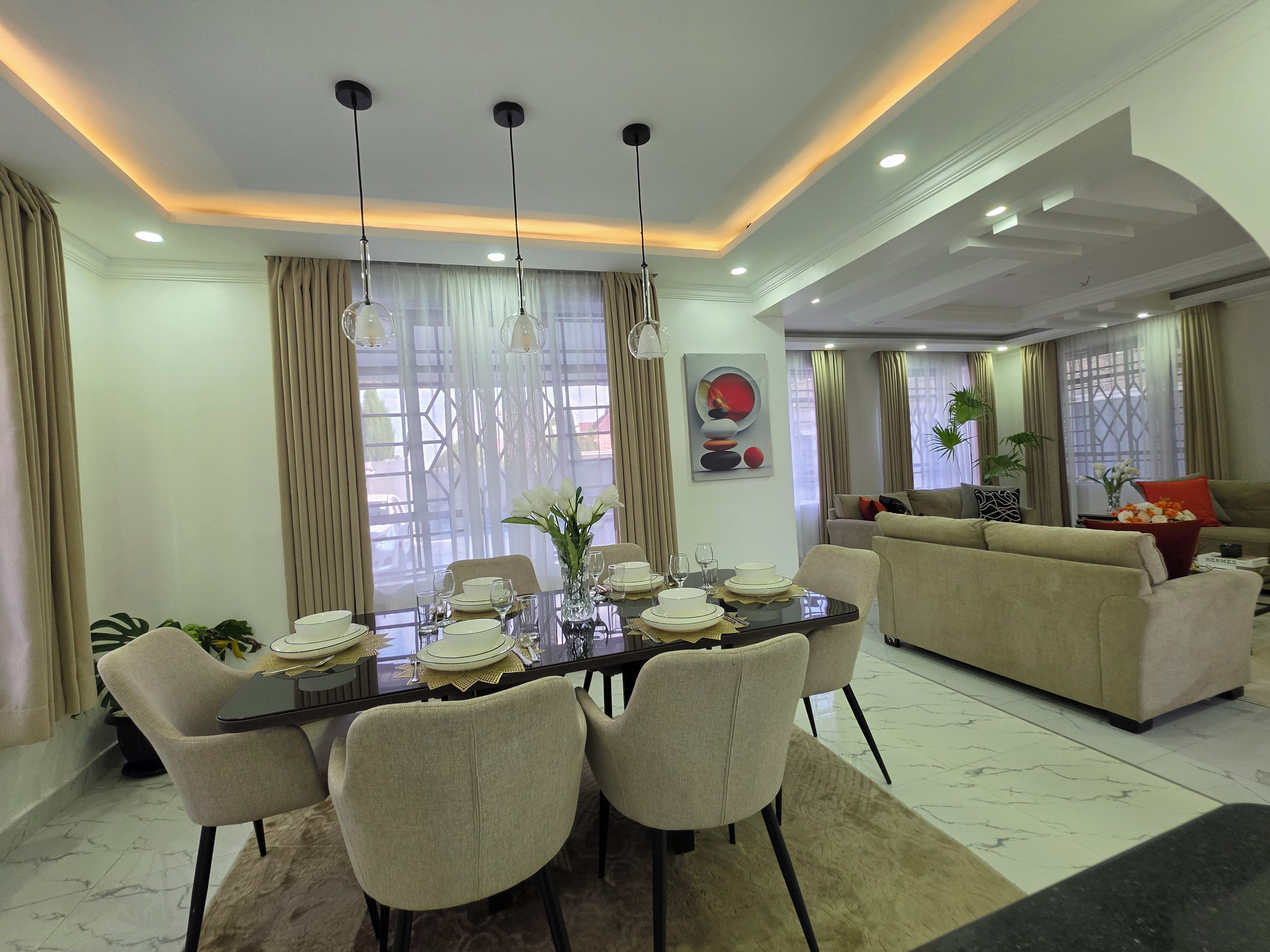 A dining area with a table set for six, surrounded by chairs, and a sofa in the background.