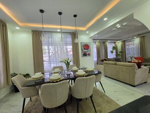A dining area with a table set for six, surrounded by chairs, and a sofa in the background. - Almara Residence Spacious 4BR Private Home (Nakuru)