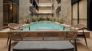 A modern atrium with a central swimming pool, surrounded by wicker furniture and a high ceiling. - Depa de lujo en Playa del carmen (Playa del Carmen)