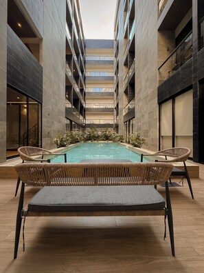Ein zeitgemäßes Atrium mit einem zentralen Schwimmbecken, umgeben von Korbmöbeln und einer hohen Decke.