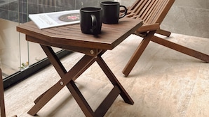A wooden lounge chair with a magazine and two black mugs on a glass table. - Depa de lujo en Playa del carmen (Playa del Carmen)