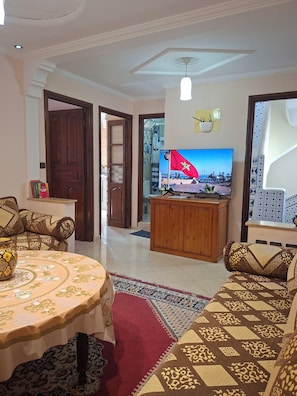 Ein Wohnzimmer mit Fernseher, Sofa, Couchtisch und einem gemusterten Teppich.