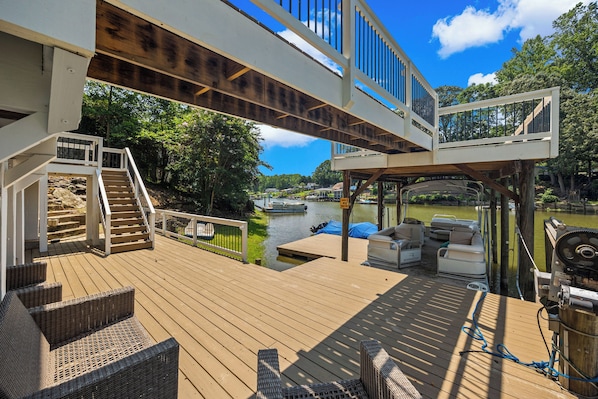 A wooden deck with outdoor furniture, a boat dock, and a river view.