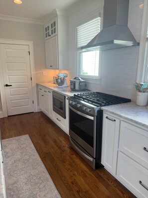 A modern kitchen with white cabinetry, a stainless steel range, an oven, and a window with blinds. - Marvelous 5-bedroom house with tons of space in 5 Points (Athens)