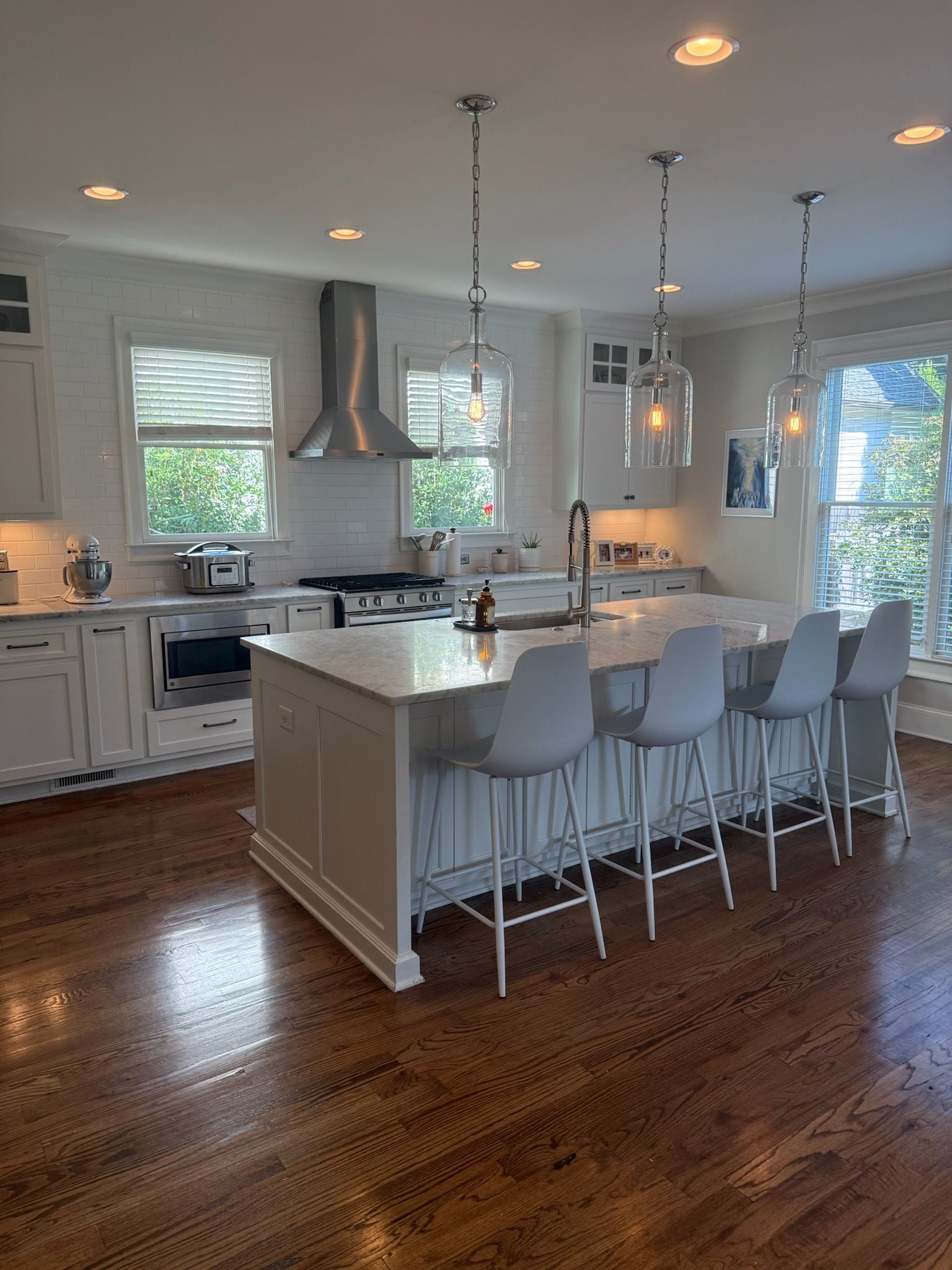 A modern kitchen with white cabinetry, a large island with bar stools, stainless steel appliances, and pendant lighting.
