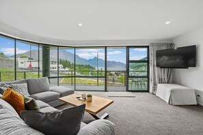A modern living room with a curved ceiling, a sofa, a coffee table, and a TV mounted on the wall. - Stunning Lake Views - Queenstown (Queenstown)